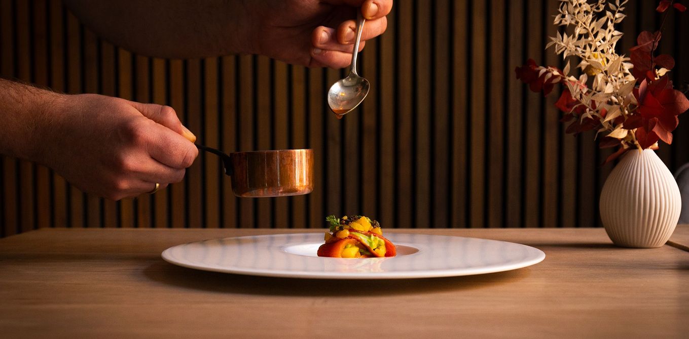 Ein Koch richtet ein Gourmet-Gericht auf einem weißen Teller an.